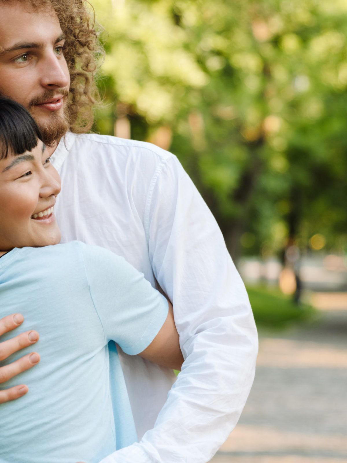 Happy young multiethnic couple cuddling embracing together in the green park close up